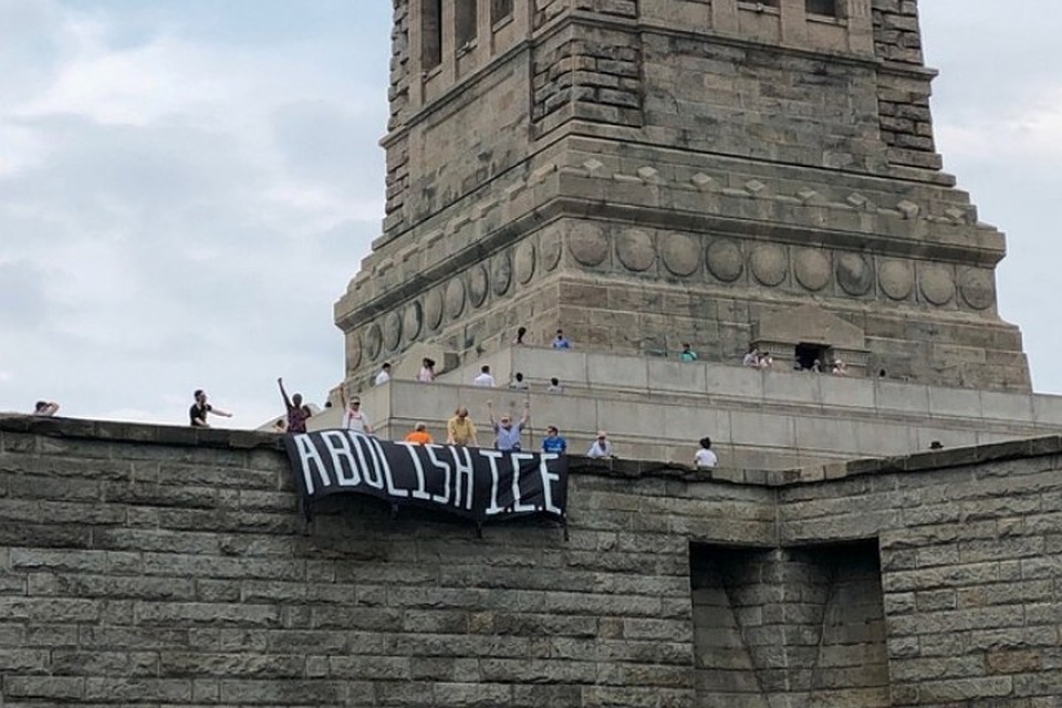 Участники акции протеста развернули у подножия статуи баннер, осуждающий иммиграционную политику Дональда Трампа