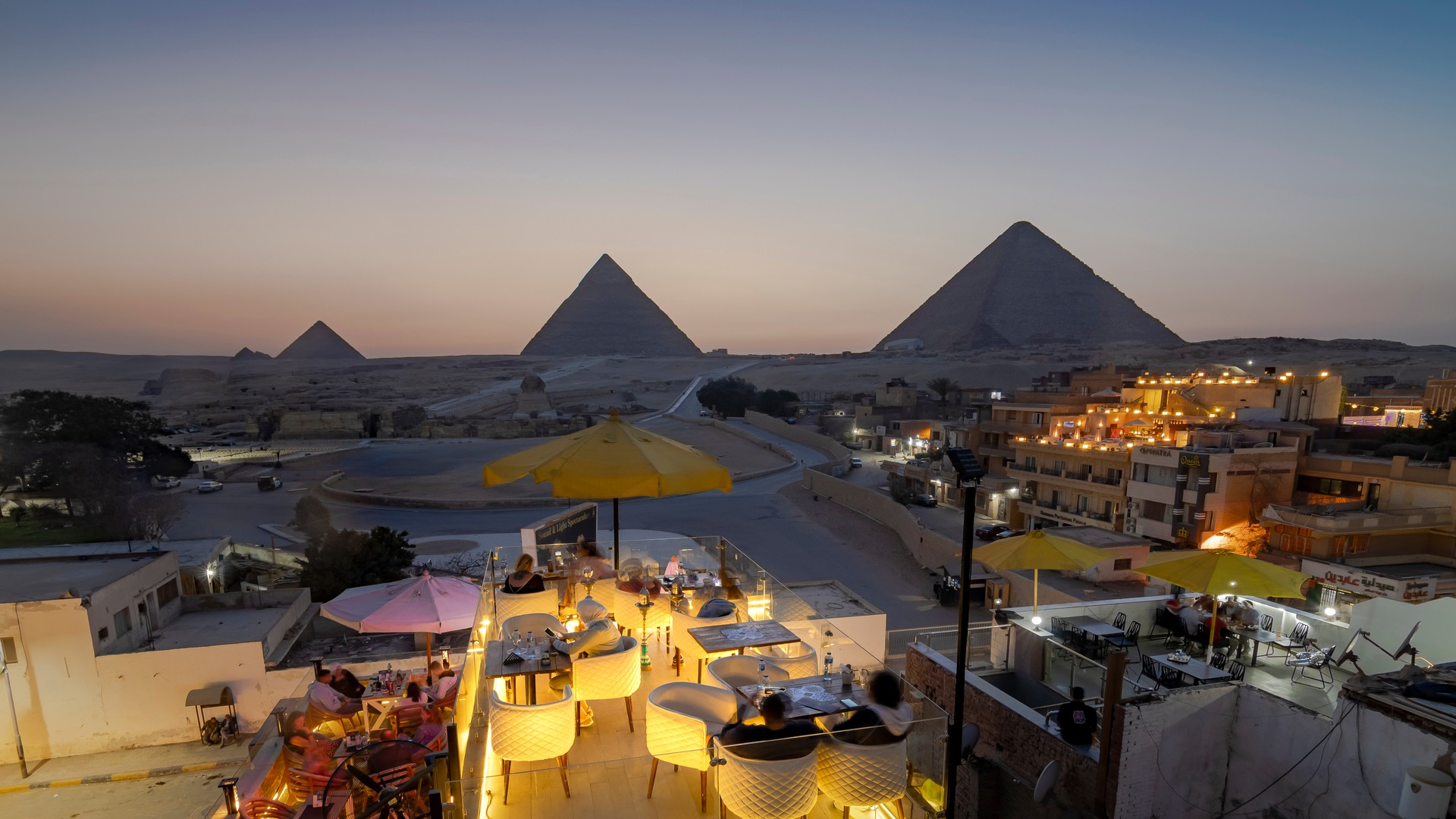 Туристы в лаунже любуются пирамидами плато Гиза на фоне заката.